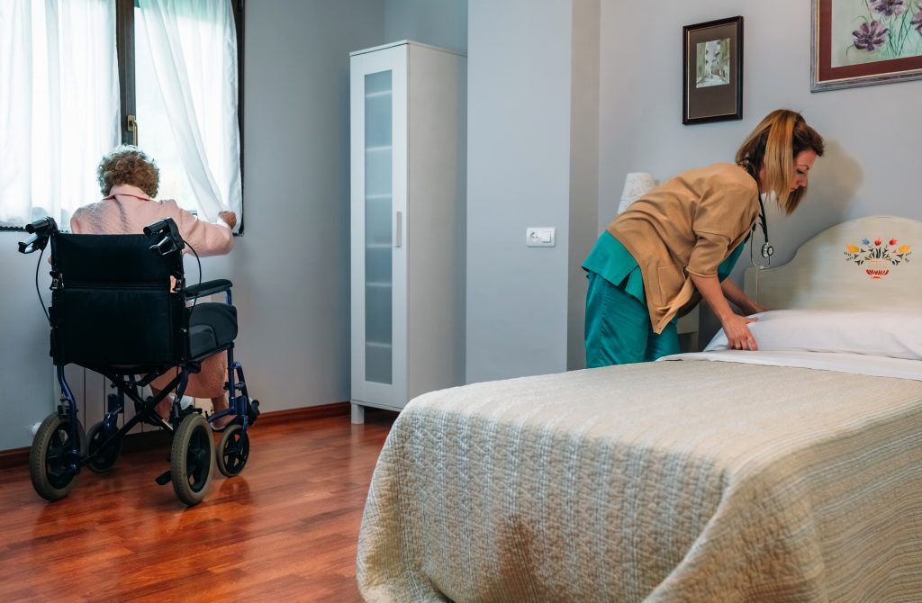 Caregiver making the bed of an elderly patient in a nursing home